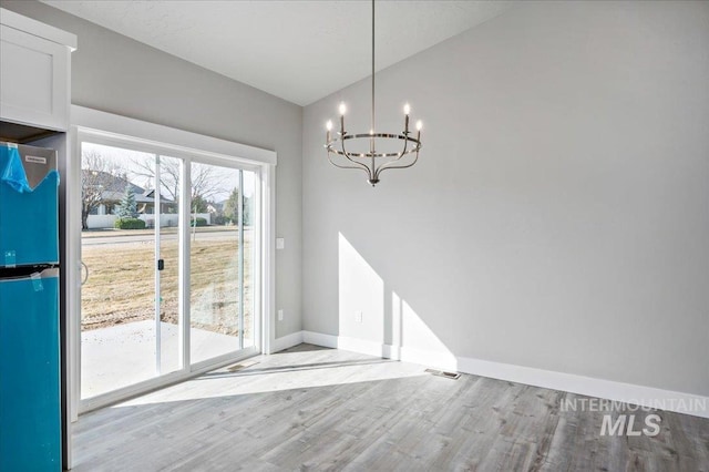 unfurnished dining area with baseboards, lofted ceiling, an inviting chandelier, and wood finished floors