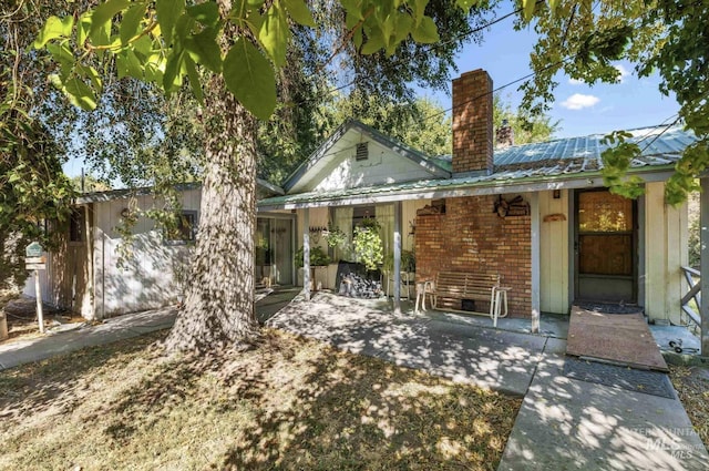 view of front of property with a patio, a chimney, metal roof, and brick siding