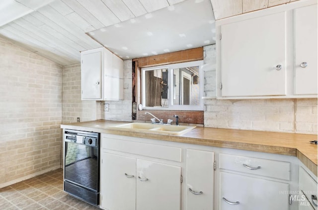 kitchen featuring white cabinets, a sink, dishwasher, light countertops, and brick wall