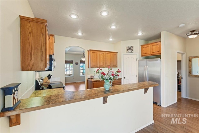 kitchen featuring a textured ceiling, appliances with stainless steel finishes, arched walkways, wood finished floors, and a peninsula