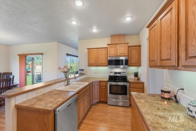 kitchen with a peninsula, a textured ceiling, appliances with stainless steel finishes, and a sink