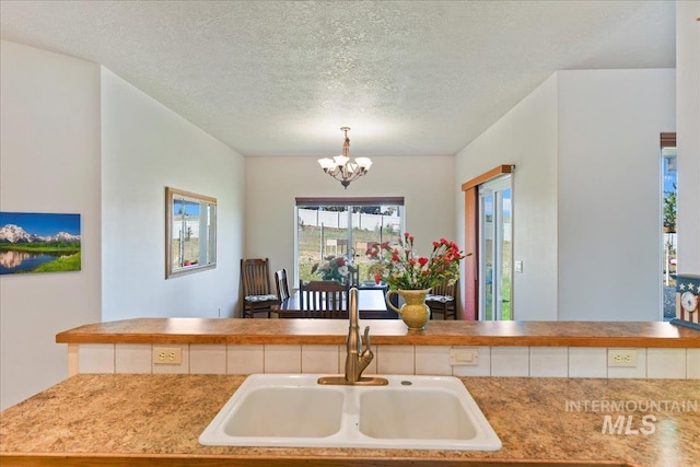 kitchen featuring decorative light fixtures, a textured ceiling, a notable chandelier, and a sink