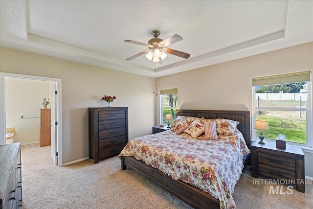 carpeted bedroom with a ceiling fan, a tray ceiling, and multiple windows