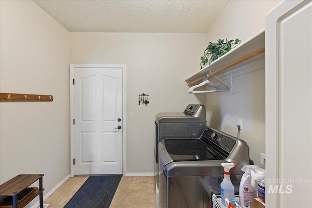 clothes washing area featuring independent washer and dryer, light tile patterned flooring, laundry area, a textured ceiling, and baseboards