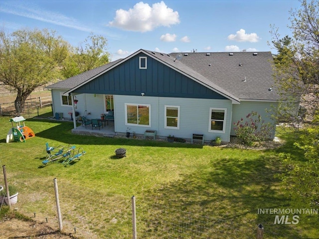 back of house with fence, roof with shingles, board and batten siding, a lawn, and a patio