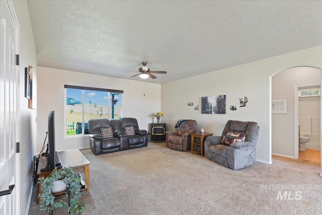 living room with carpet flooring, ceiling fan, a textured ceiling, arched walkways, and a wealth of natural light