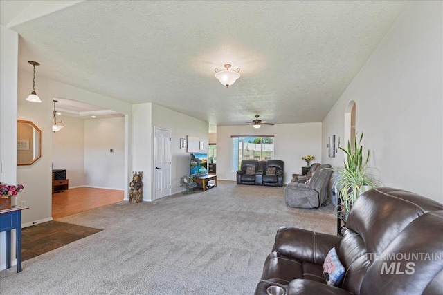 living room featuring carpet flooring, arched walkways, a textured ceiling, a ceiling fan, and baseboards