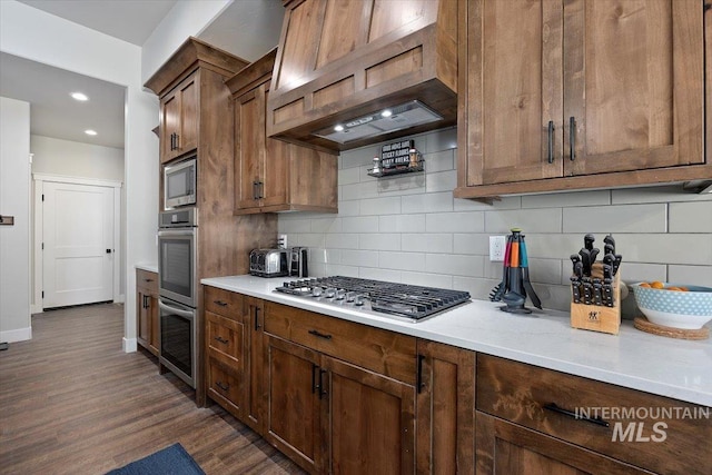 kitchen featuring baseboards, appliances with stainless steel finishes, backsplash, dark wood-style floors, and custom range hood