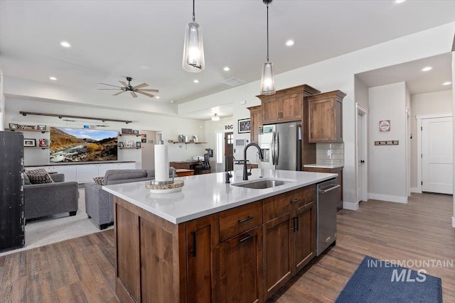 kitchen featuring a kitchen island with sink, a sink, open floor plan, light countertops, and appliances with stainless steel finishes