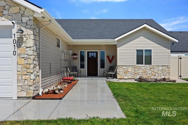 property entrance featuring an attached garage, stone siding, a shingled roof, and a lawn