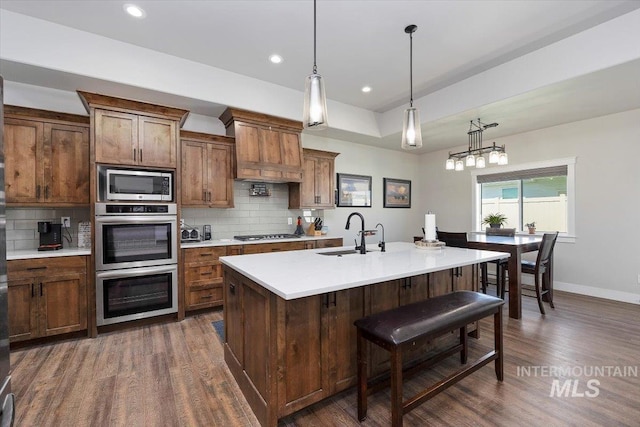 kitchen with light countertops, a sink, decorative light fixtures, and an island with sink