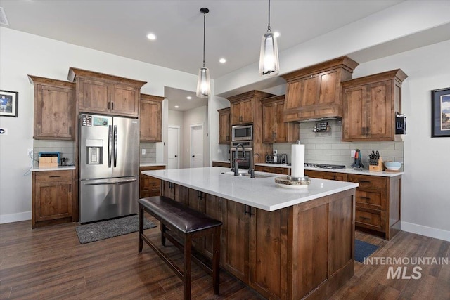 kitchen featuring decorative light fixtures, a sink, light countertops, appliances with stainless steel finishes, and a center island with sink