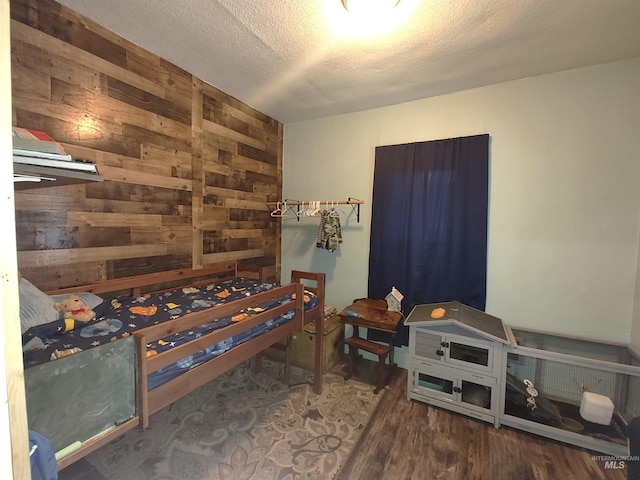 bedroom with hardwood / wood-style flooring, wooden walls, and a textured ceiling