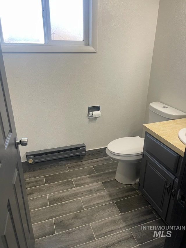 bathroom with wood finish floors, a baseboard radiator, toilet, and vanity