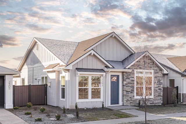 view of front facade featuring a shingled roof, board and batten siding, and fence