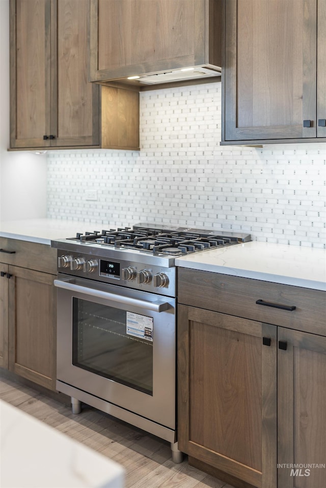 kitchen with light countertops, stainless steel gas range, light wood-style flooring, and decorative backsplash