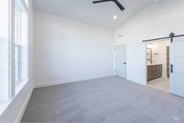 unfurnished bedroom with light carpet, a barn door, high vaulted ceiling, and baseboards