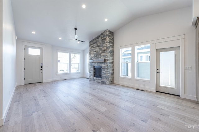 unfurnished living room with lofted ceiling, visible vents, a stone fireplace, and light wood finished floors