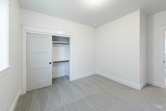 unfurnished bedroom featuring baseboards, a closet, and light colored carpet