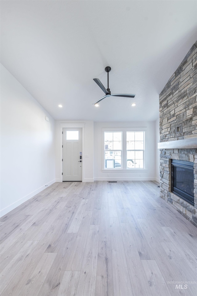 unfurnished living room featuring a stone fireplace, light wood-style flooring, recessed lighting, a ceiling fan, and baseboards