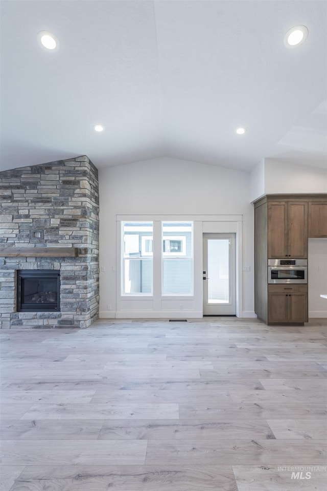 unfurnished living room featuring a stone fireplace, recessed lighting, baseboards, vaulted ceiling, and light wood finished floors