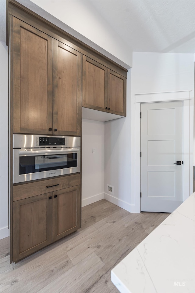 kitchen featuring oven, visible vents, baseboards, light stone countertops, and light wood finished floors