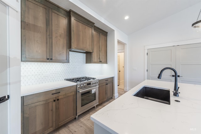 kitchen with tasteful backsplash, light stone counters, high end stainless steel range, vaulted ceiling, and a sink