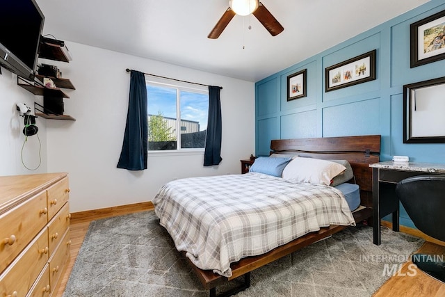 bedroom with a decorative wall, baseboards, ceiling fan, and wood finished floors