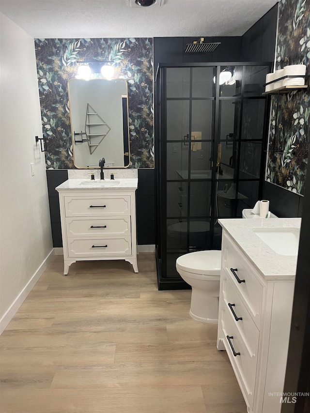 bathroom featuring wood-type flooring, toilet, vanity, and a shower with shower door