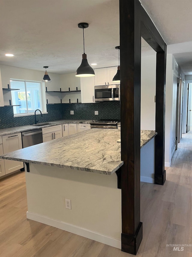 kitchen featuring light wood finished floors, a sink, appliances with stainless steel finishes, and open shelves