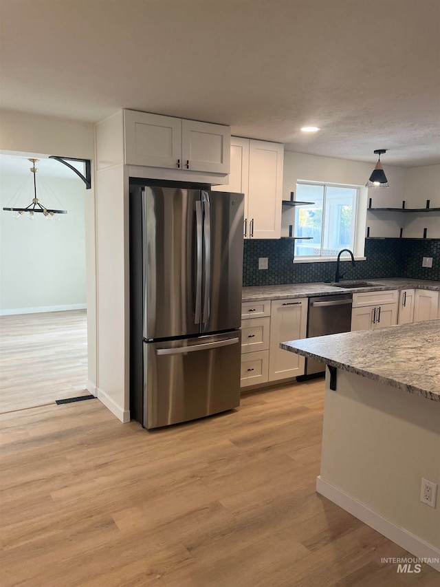 kitchen featuring a sink, open shelves, light wood-type flooring, stainless steel appliances, and decorative backsplash