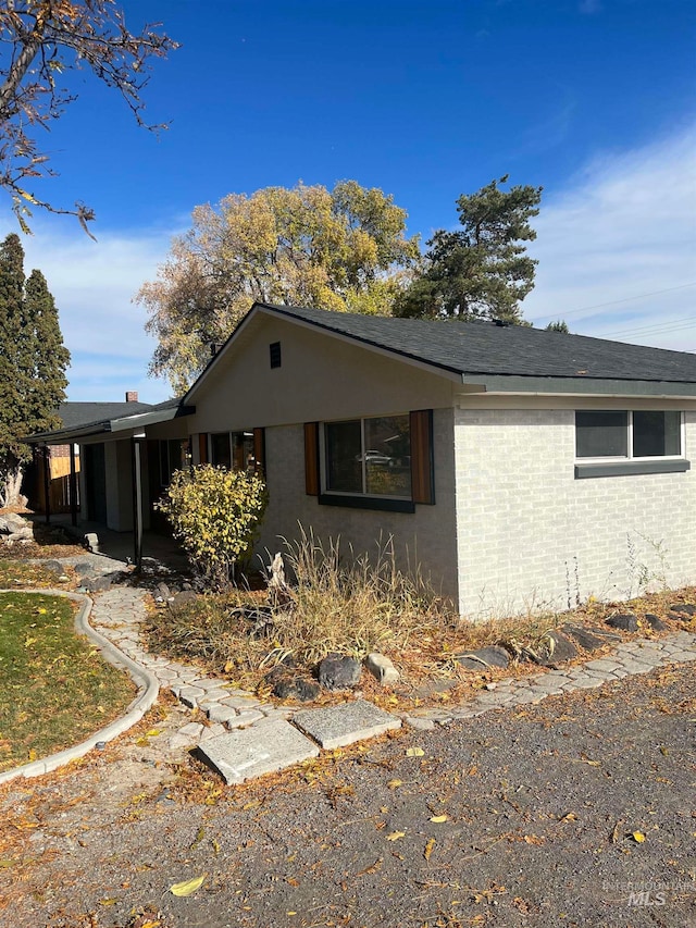 view of side of home featuring a shingled roof and brick siding