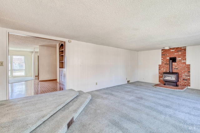 unfurnished living room featuring a wood stove, visible vents, a textured ceiling, and carpet flooring