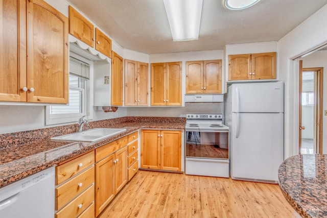 kitchen with under cabinet range hood, white appliances, a sink, light wood finished floors, and dark stone countertops