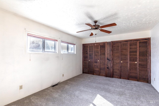 unfurnished bedroom with carpet floors, a textured ceiling, multiple closets, and a ceiling fan