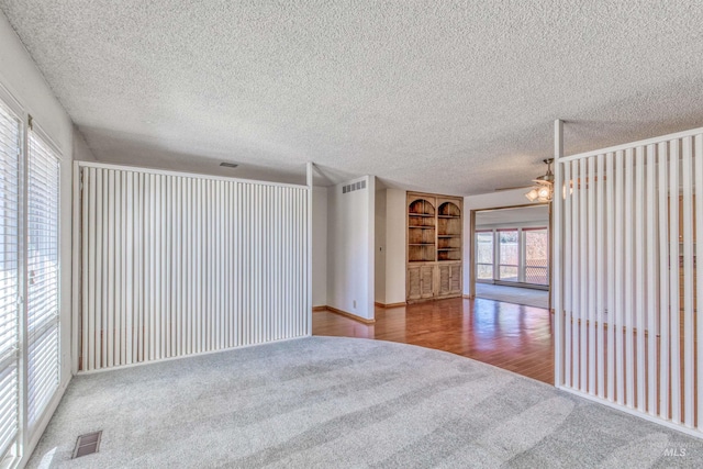 carpeted spare room featuring built in features, visible vents, a textured ceiling, and wood finished floors