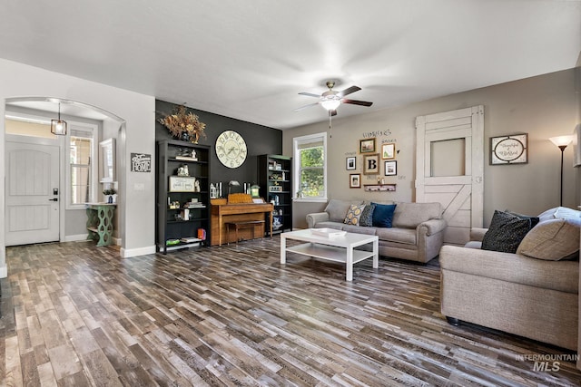 living area with arched walkways, wood finished floors, a ceiling fan, and baseboards