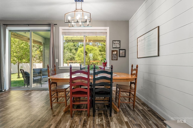 dining space with plenty of natural light, dark wood finished floors, wood walls, and a chandelier