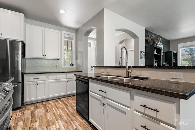 kitchen featuring a sink, dark stone counters, tasteful backsplash, appliances with stainless steel finishes, and light wood-style flooring