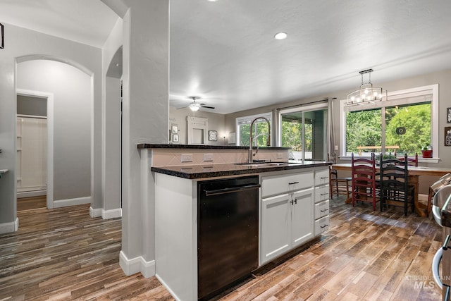 kitchen with a sink, wood finished floors, dishwasher, arched walkways, and dark countertops