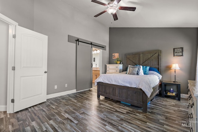 bedroom with a barn door, dark wood finished floors, baseboards, high vaulted ceiling, and connected bathroom