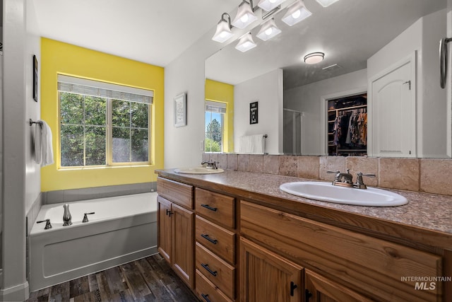 full bath with wood finished floors, double vanity, a garden tub, a shower, and a spacious closet