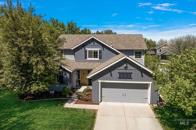 traditional-style home with board and batten siding, concrete driveway, a front yard, a garage, and roof with shingles