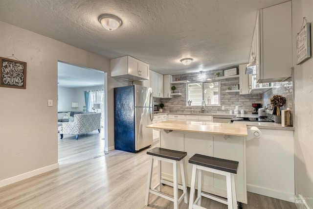 kitchen featuring a sink, a peninsula, freestanding refrigerator, open shelves, and backsplash