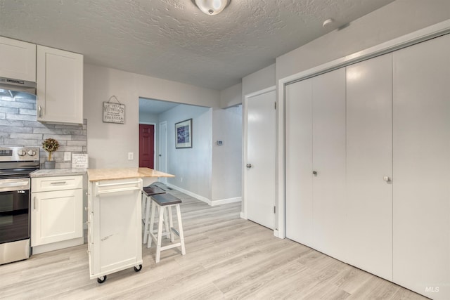 kitchen featuring under cabinet range hood, white cabinetry, stainless steel range with electric cooktop, light countertops, and light wood-type flooring