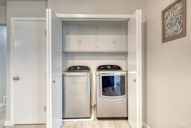 clothes washing area with light wood finished floors, cabinet space, and washer and clothes dryer