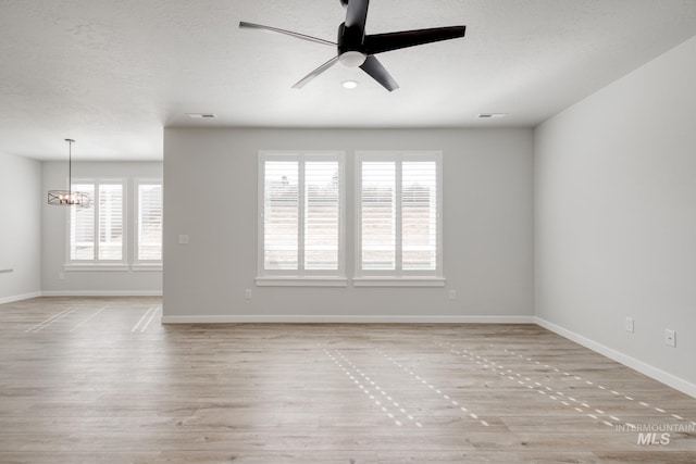 spare room featuring ceiling fan with notable chandelier, wood finished floors, and baseboards