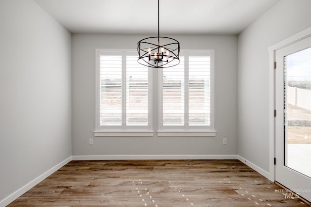 unfurnished dining area featuring an inviting chandelier, baseboards, wood finished floors, and plenty of natural light