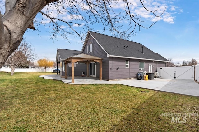 back of property with a patio, a shingled roof, fence, a lawn, and a gate