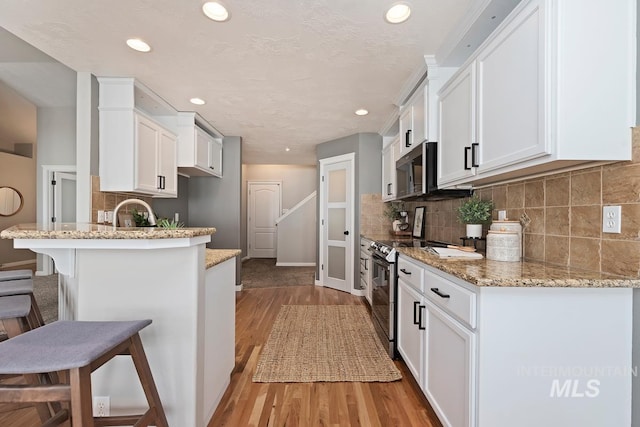 kitchen featuring stainless steel appliances, white cabinets, a peninsula, and a kitchen breakfast bar